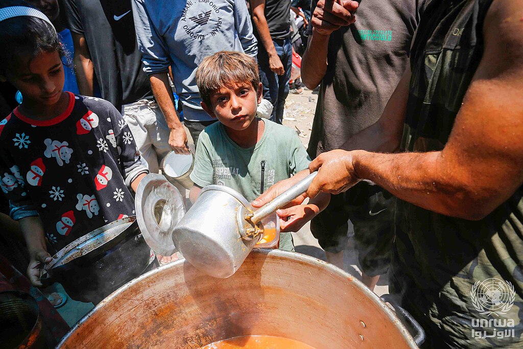1024px Displaced Palestinians gather to receive food from a charity in Deir el Balah Gaza Strip