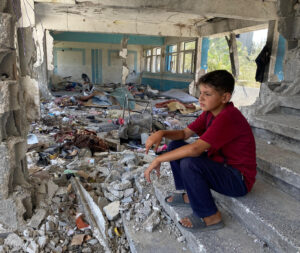 طفل يجلس على أنقاض مدرسة مدمرة تابعة للأمم المتحدة في غزة، الصورة: الأونروا