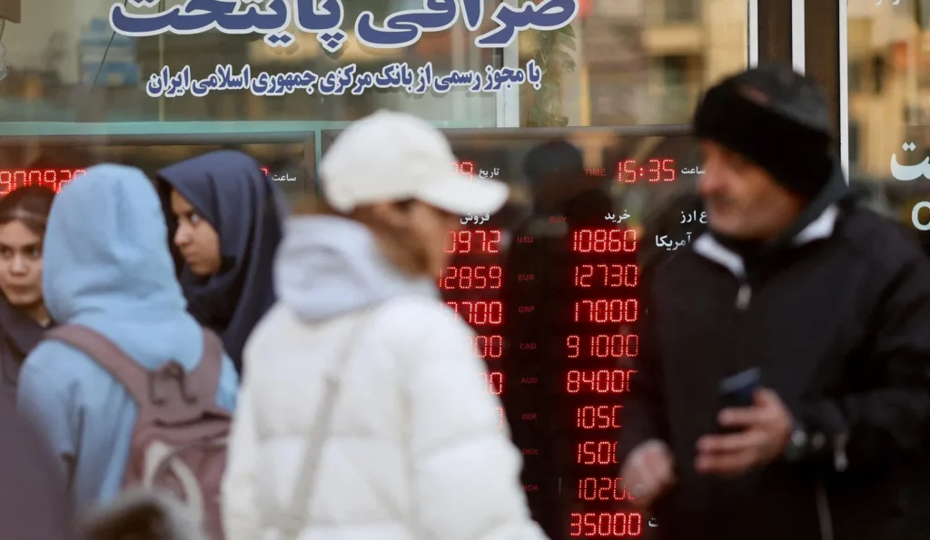 مواطنون إيرانيون يسيرون أمام لوحة تعرض أسعار صرف العملات في طهران. تصوير: ماجد أصغري بور/ رويترز.